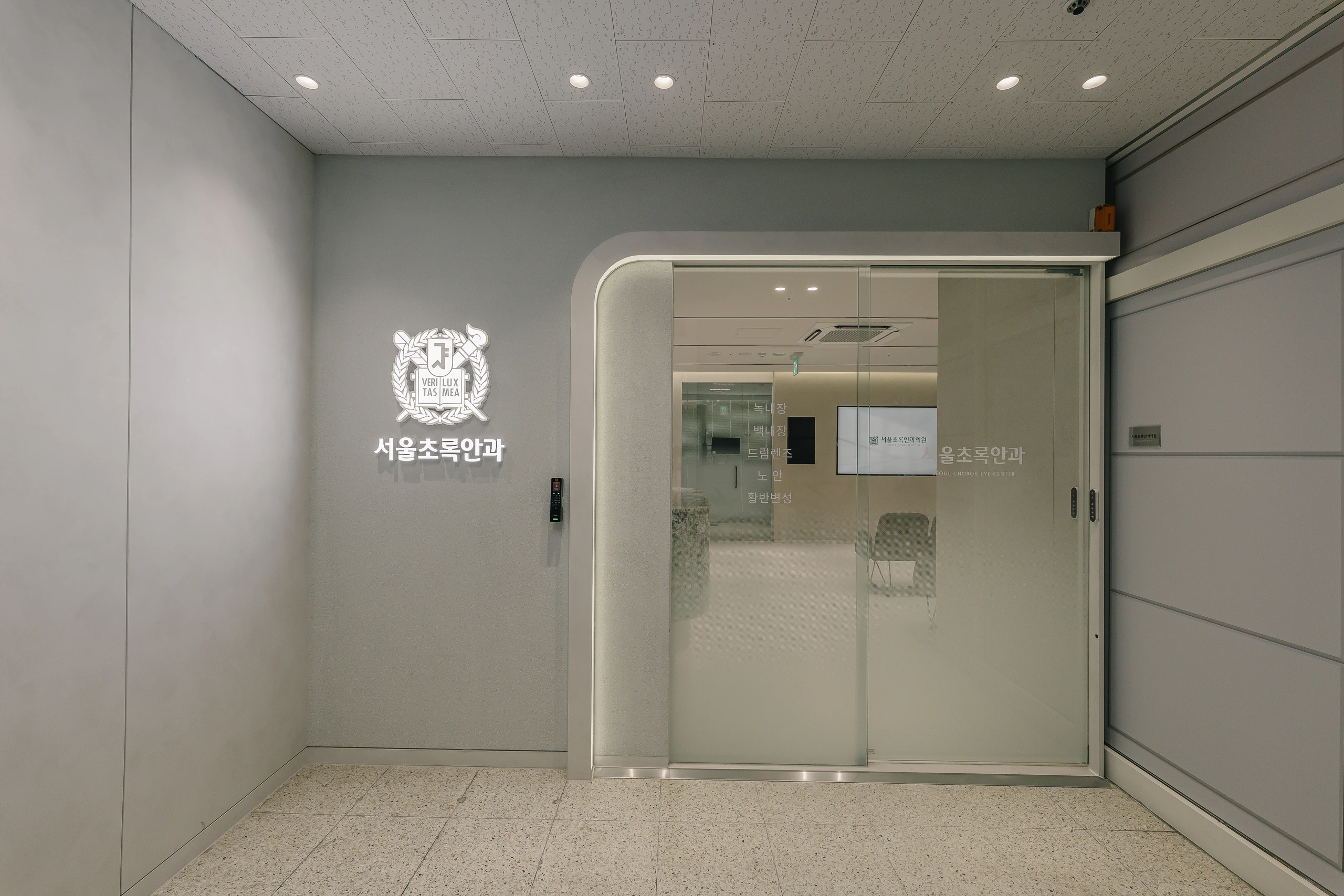 서울초록안과 입구. 벽면 로고 사인과 유리 자동문, 문 너머로 안쪽 공간이 보인다.